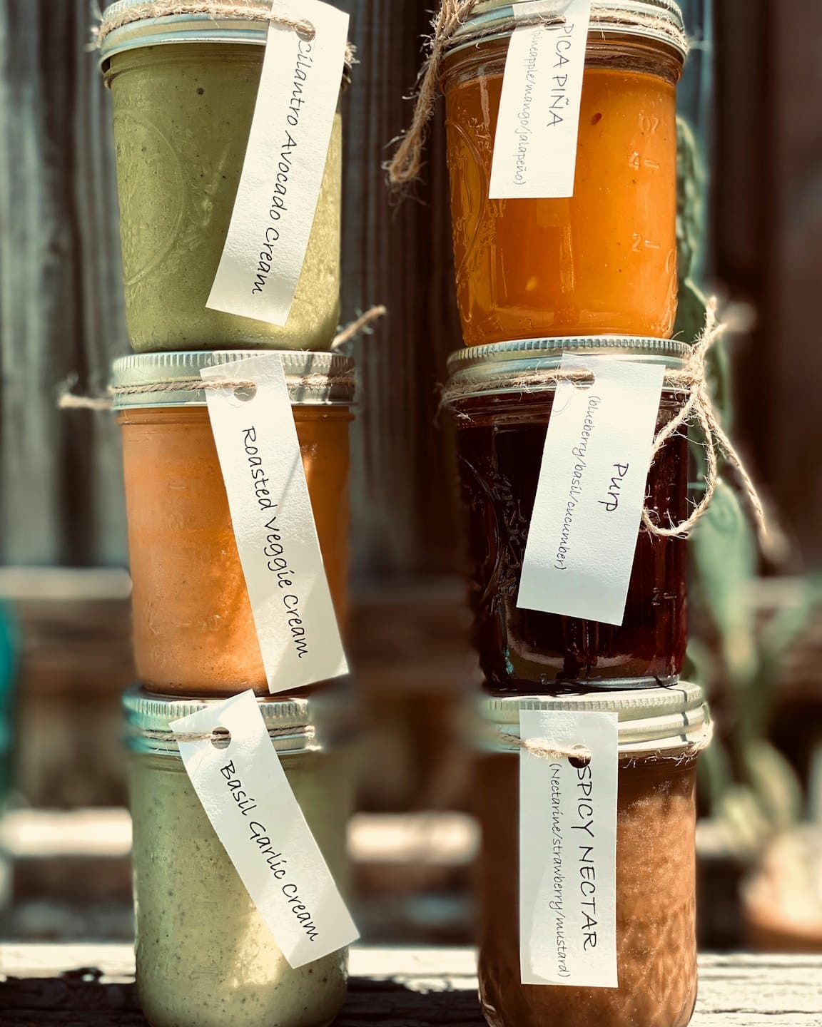 Six glass jars with handwritten labels stacked outdoors.