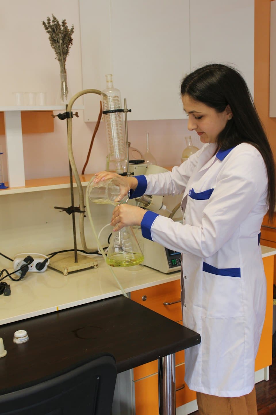 Scientist in a lab coat pours liquid into a glass flask.